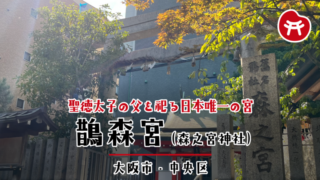 鵲森宮の石の鳥居としめ縄、右手に「森之宮」と刻まれた社号標、奥に朱色の社殿と背後のビル
